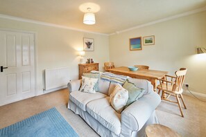 A cozy living room with a sofa, a dining table, and a chair. There is a radiator, a lamp, and a picture on the wall. - Host and Stay - The Cottage ALN (Alnwick)