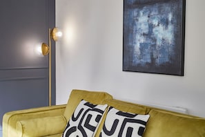 A yellow sofa with patterned cushions, a floor lamp, and a piece of abstract art on the wall. - Host Stay - The Premier Loft (Middlesbrough)