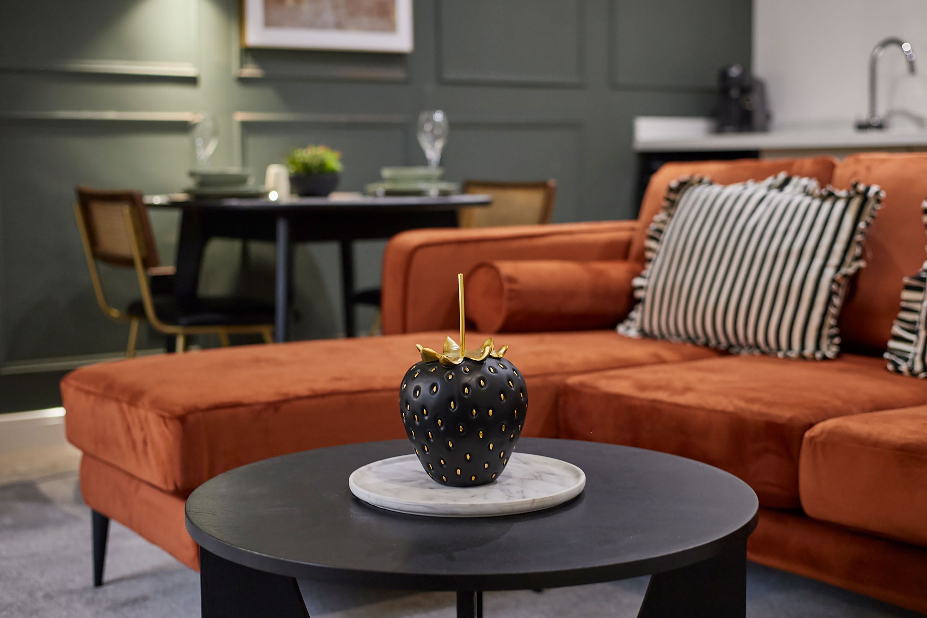 Un salon moderne avec une table basse noire, un canapé agrémenté de coussins à rayures et un vase décoratif noir orné de motifs dorés.