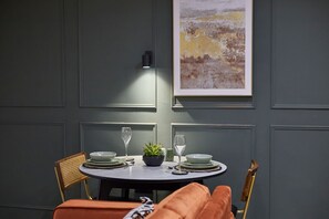 A dining area with a round table set for two, featuring a potted plant, wine glasses, and plates. - Host Stay - The Executive Suite (Middlesbrough)