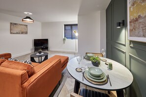 A modern living room with a sofa, a television, a dining table set with plates, glasses, and a plant. - Host Stay - The Executive Suite (Middlesbrough)