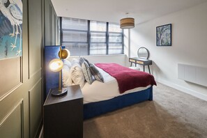 Ein Schlafzimmer mit Bett, Nachttisch, Lampe, Fenster und Kunstwerk.