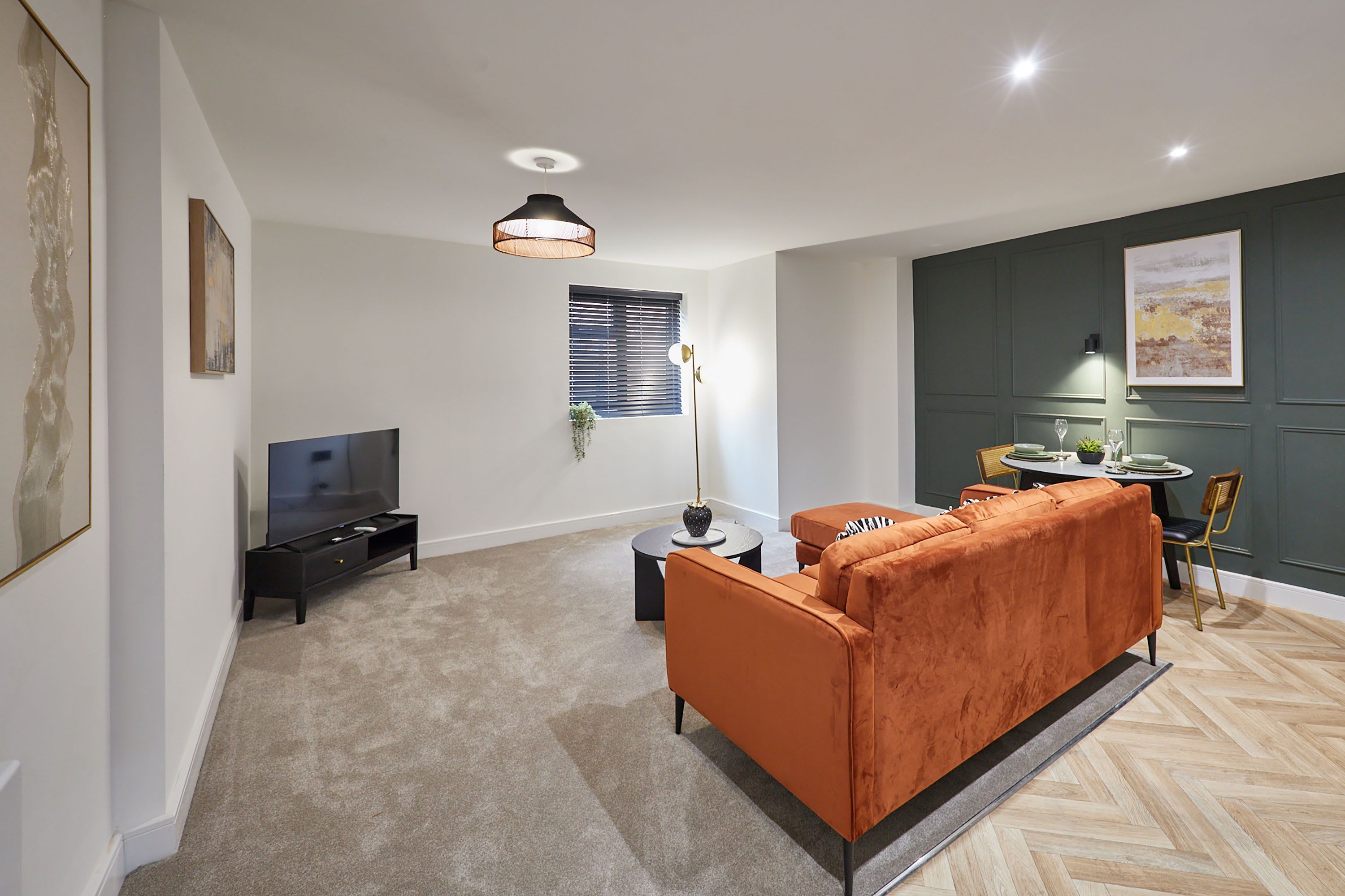 A modern living room with a flat-screen TV, orange sofa, and a dining area with a table and chairs.
