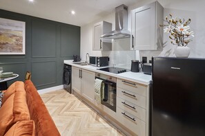 Eine moderne Küche mit weißen Schränken, einem schwarzen Kühlschrank und einem Essbereich mit einer Couch.