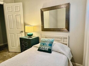 A bedroom with a bed, a nightstand with a lamp, a mirror, and a door. - Tiny 30A Stay - Walk to Beach Dining Trails (Santa Rosa Beach)