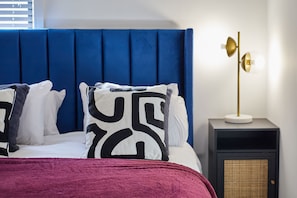 A bed with a blue headboard, white and patterned pillows, a red blanket, and a bedside table with a lamp. - Host Stay - The Signature Suite (Middlesbrough)