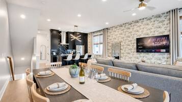 A modern living room with a dining area, a flat-screen TV mounted on the wall, and a ceiling fan.