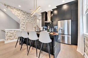 Cozinha moderna com armários escuros, uma ilha central com banquetas e uma luminária decorativa.