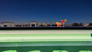 A rooftop bar with a city skyline view, green stools, and two cocktails.