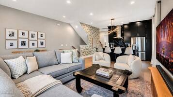 A modern living room with a grey sofa, a coffee table, and a TV screen displaying a concert.