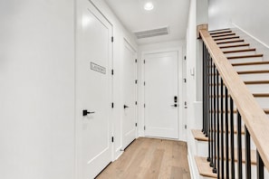 Ein Flur mit weißen Türen, eine davon mit der Beschriftung 'LAUNDRY', der zu einer Treppe mit Holzboden und schwarzen Geländern führt.