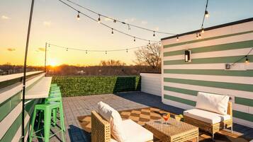 An outdoor patio with green-striped walls, wicker furniture, and string lights.