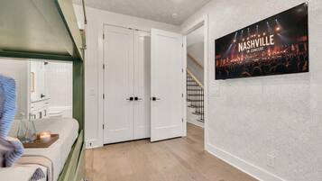 A hotel room with a bed, a bedside table with a lamp, a TV on the wall, and a door leading to another room.