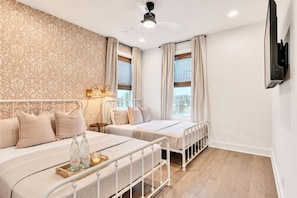 Ein Schlafzimmer mit zwei Betten, einem Deckenventilator, einem an der Wand montierten Fernseher und einem Fenster mit Vorhängen.