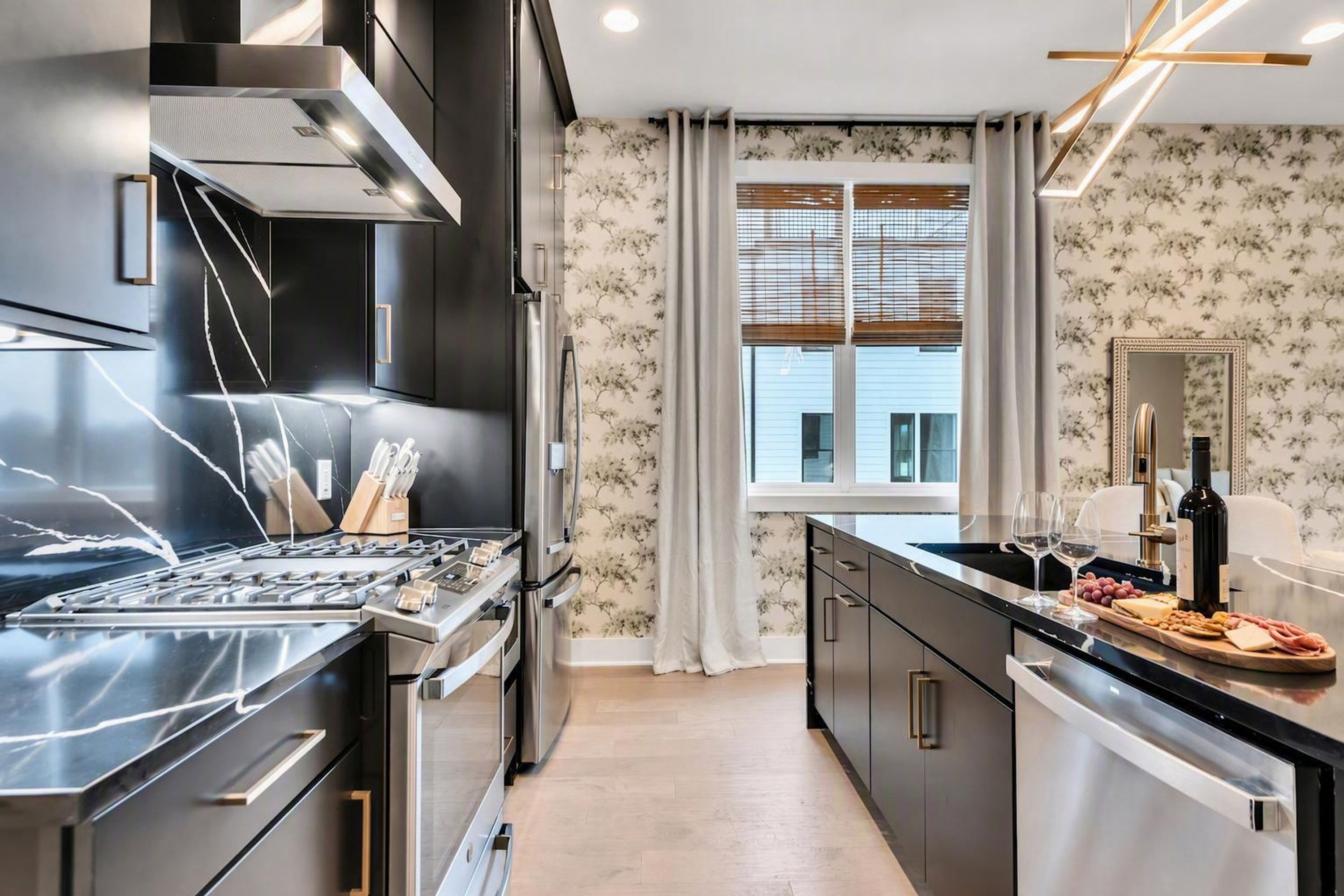A modern kitchen with stainless steel appliances, a wooden cutting board with food, and a window with blinds.