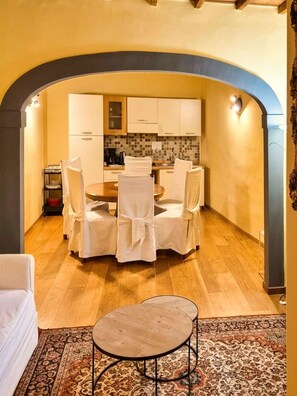 Ein Essbereich mit rundem Tisch und Stühlen, im Hintergrund eine Küche und ein gemustertes Teppich.