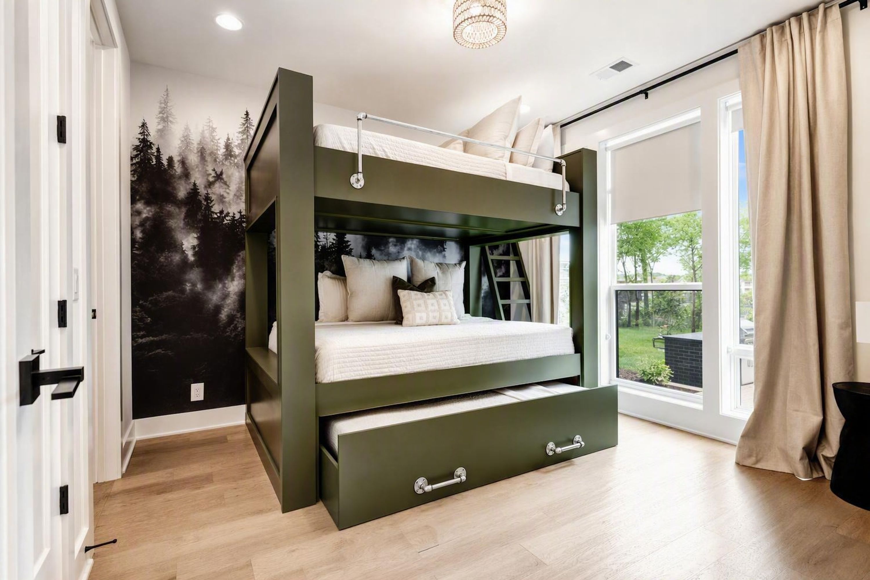 A bunk bed with a lower bunk drawer, a forest mural on the wall, and a sliding glass door to the outside.