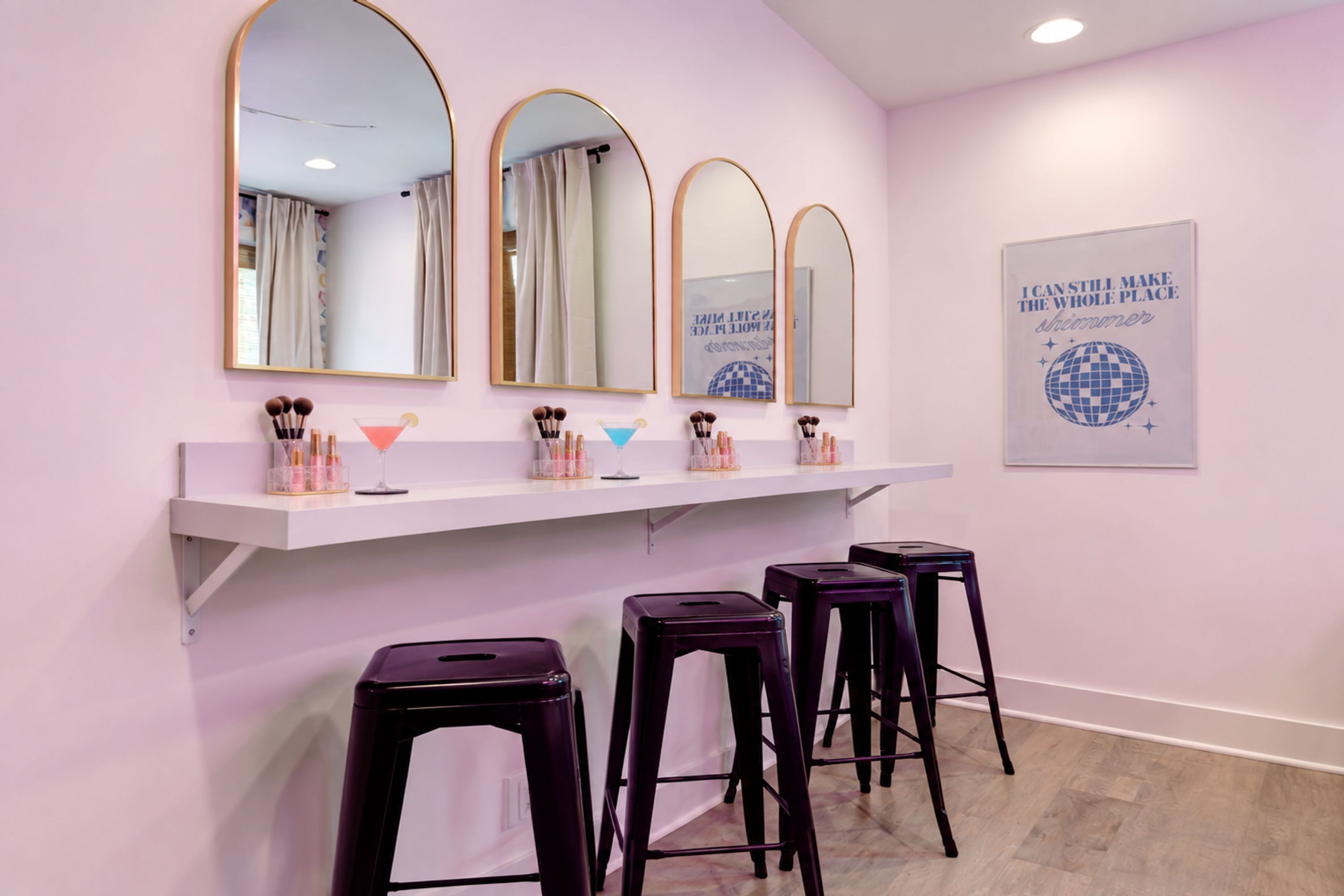 A salon with three mirrors, a vanity with makeup brushes, and a poster on the wall.
