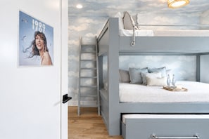 Een stapelbed met een ladder, een nachtkastje met flessen en een poster aan de muur.