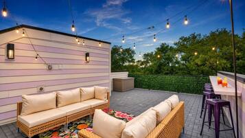 Een terras buiten met een bank, een bar en lichtslingers.