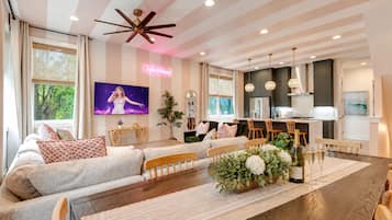 A modern living room with a large flat-screen TV, a ceiling fan, and a dining area with a wooden table and chairs.