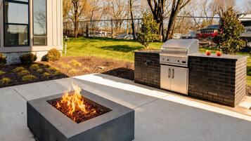 An outdoor kitchen with a built-in grill, a fire pit, and a brick wall.