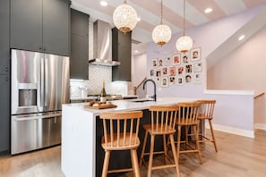Een moderne keuken met roestvrijstalen apparatuur, een centraal kookeiland met barkrukken en decoratieve verlichting.
