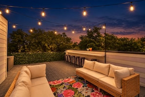 Een terras buiten met een bank, een eettafel en lichtslingers.