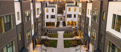 Un moderno complejo de apartamentos con un patio central, varios balcones y un horizonte urbano al fondo.