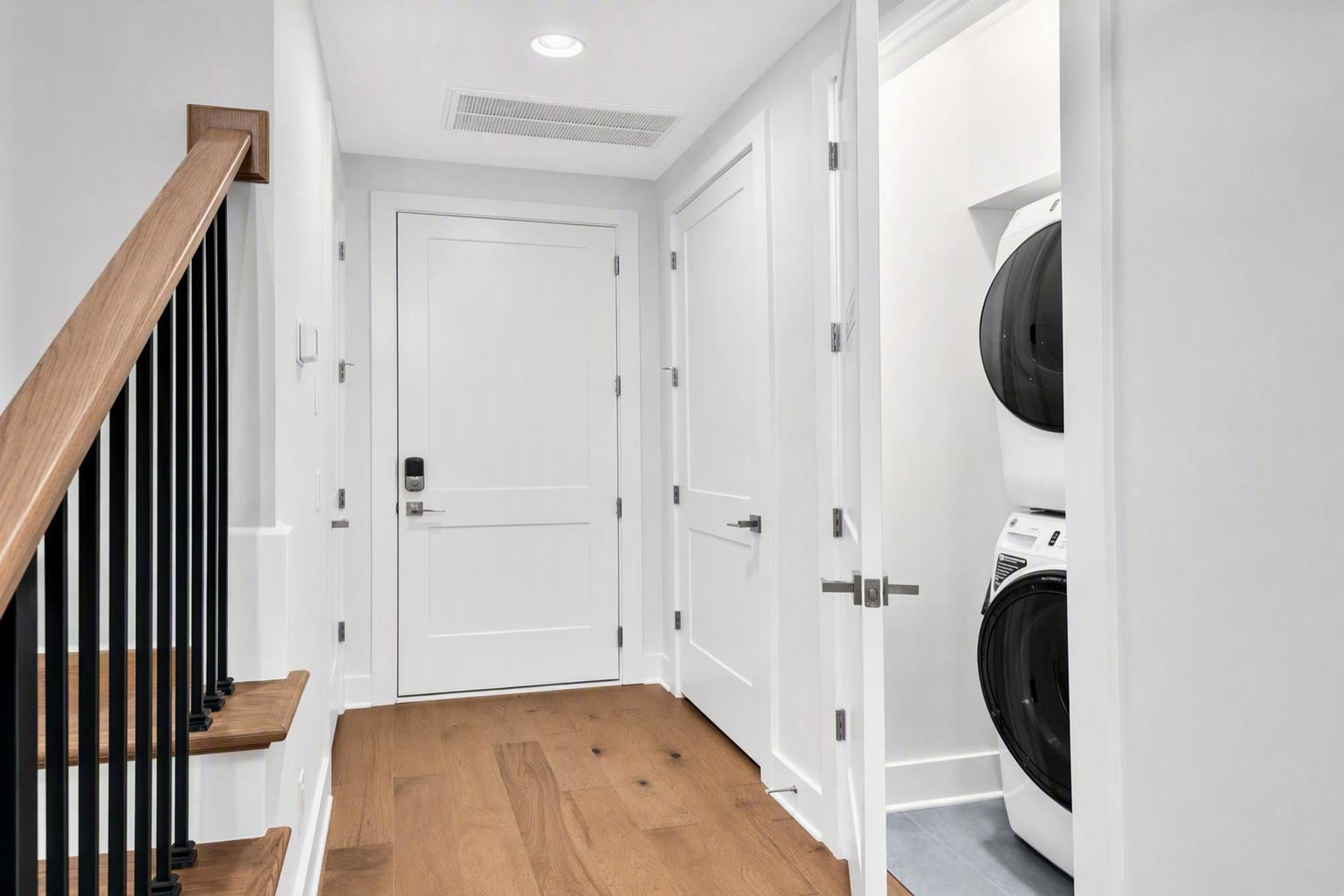 A hallway with a wooden staircase, a white door, and a laundry area with a washing machine.