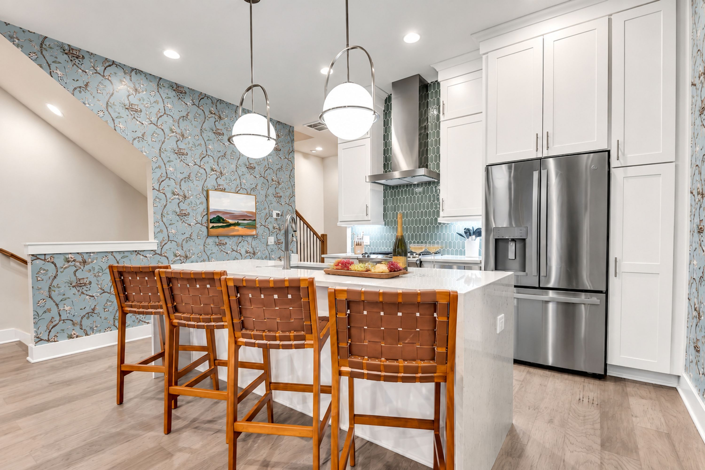 Una cocina con una isla central, sillas de madera, un refrigerador de acero inoxidable y una escalera con un detalle decorativo en la pared.