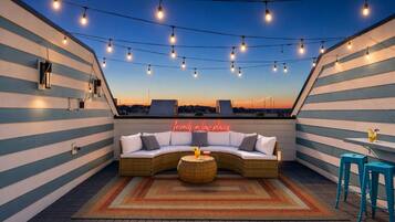 Une terrasse sur le toit avec un canapé incurvé, une table ronde et des guirlandes lumineuses.
