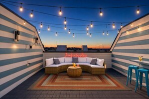 Una terraza en la azotea con un sofá curvo, una mesa redonda y luces colgantes.