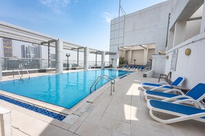 Ein Pool auf dem Dach mit blau gefliesten Rändern, einer Metalltreppe und blauen Liegestühlen.