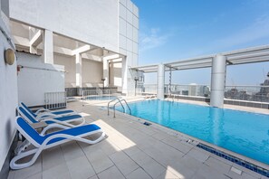 Ein Pool auf dem Dach mit Liegestühlen und Blick auf die Skyline der Stadt.