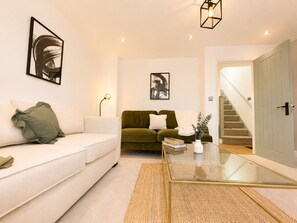 A modern living room with a white sofa, a green sofa, a glass coffee table, and artwork on the walls. - Perfect Booking Modern 4-bed Home With Garden (Windsor)