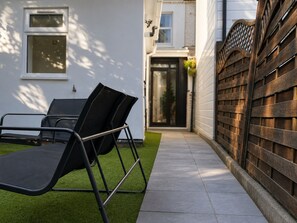 A patio with a black metal chair and a table, a wooden fence, and a house with a door and windows. - Perfect Booking Modern 4-bed Home With Garden (Windsor)