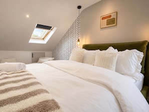 A modern bedroom with a skylight, a green upholstered headboard, and a herringbone-patterned wall. - Perfect Booking Modern 4-bed Home With Garden (Windsor)