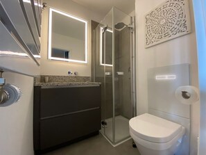Ein modernes Badezimmer mit einer gläsernen Duschkabine, einer weißen Toilette und einem Waschtisch mit Spiegel.