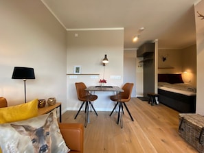 Ein kompakter Wohnraum mit Essbereich, einer Couch, einer Lampe und einem Bett, an der Wand ein montiertes Tiergeweih.