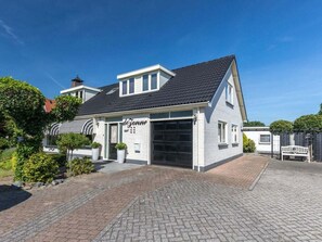 A two-story building with a garage, surrounded by a paved driveway and greenery. - Holiday Home in Renesse With Swimming Pool (Renesse)