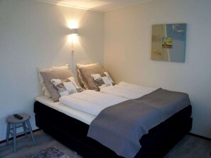 A bedroom with a bed, a nightstand, a wall-mounted lamp, and a painting. - Holiday Home in Renesse With Swimming Pool (Renesse)