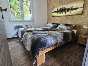 Ein Schlafzimmer mit einem hölzernen Bett, einem Heizkörper, einem Fenster mit Blick auf Bäume und einem Wandbild.