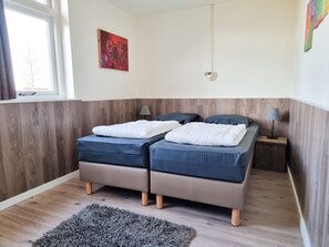 Ein Doppelbett mit weißer Decke und zwei Kissen, ein Nachttisch mit Lampe, ein kleiner Teppich und ein Bild an der Wand.