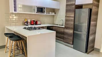 A modern kitchen with white cabinets, a stainless steel refrigerator, a microwave, and a gas stove.