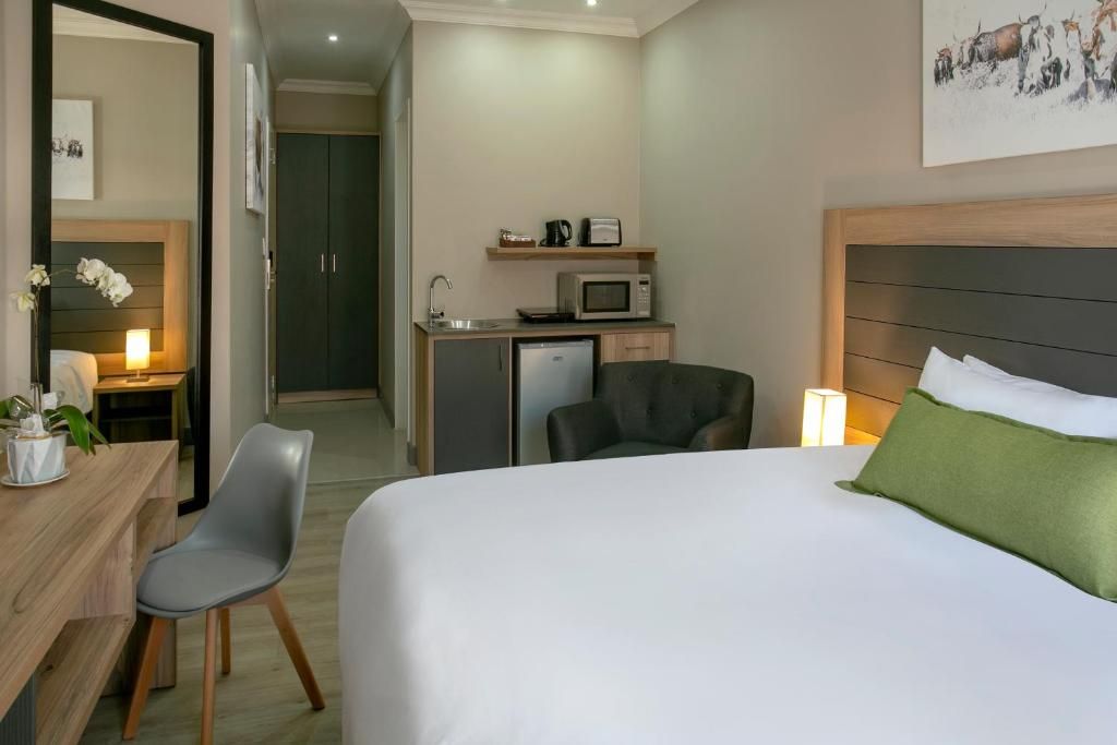 Habitación de hotel con cama, escritorio con silla, una kitchenette pequeña y un baño a la vista.