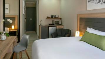 Habitación de hotel con cama, escritorio con silla, una kitchenette pequeña y un baño a la vista.