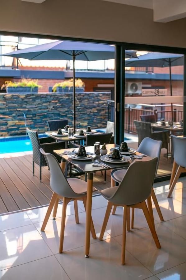 Un espacio de comedor al aire libre con vista a una piscina y un muro de piedra.