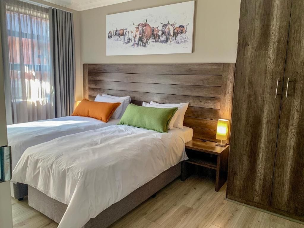 A hotel room with two beds, a wooden headboard, a nightstand with a lamp, and a large painting on the wall.