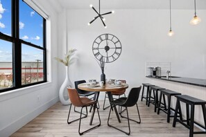 A modern dining area with a round table, chairs, a large wall clock, and pendant lights. - Lux Stay Near NYC - Patio, Gym & Free Parking (Kearny)